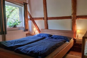 Ein Schlafzimmer mit Bett, einem Fenster mit Vorhängen, einem Heizkörper und Holzbalken.