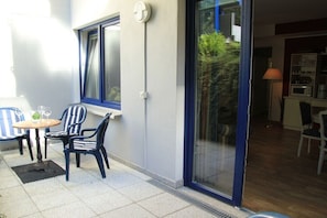 Eine Terrasse mit Tisch und Stühlen, eine Glasschiebetür und Blick ins Grüne.