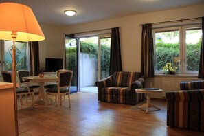 Ein Wohnzimmer mit Esstisch, Stühlen, Sofas, einem Fernseher und einer Glasschiebetür, die in einen Garten führt.