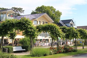 Ein Gebäude mit gelber Fassade, einem Balkon und einem Gartenbereich mit Bänken und einer weißen Struktur.
