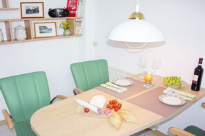 Ein Essbereich mit einem für zwei Personen gedeckten Tisch, mit Käseplatte, Brot und einer Weinflasche.