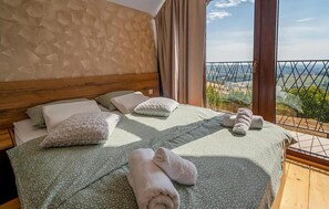 Ein Bett mit Kissen und Handtüchern, ein hölzernes Kopfteil und Blick auf die Landschaft durch ein Fenster.