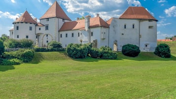 A large, historic building with multiple towers and a well-maintained lawn in front.