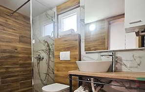 Ein Badezimmer mit Holzvertäfelung, einem weißen Waschbecken und einer Glasdusche.
