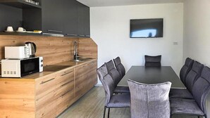 A modern kitchen with a microwave, sink, and wooden cabinets. There is a dining area with a table and chairs. A flat-screen TV is mounted on the wall. - 3 bedroom cozy home in Kalnik (Kalnik)