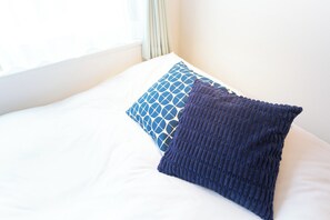 Ein Bett mit weißer Bettwäsche und zwei Kissen, eines mit geometrischem Muster, das andere gestrickt.