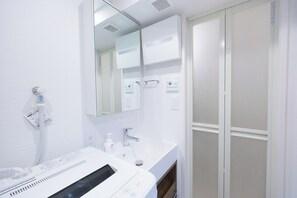 Ein modernes Badezimmer mit einem weißen Waschbecken, einem Spiegel, einer Duschbrause und einem Handtuchhalter.