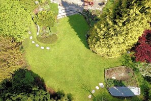 Una vista aerea di un giardino con prato, alberi e un piccolo spazio relax.