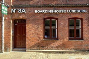 Ein Backsteinhaus mit einer großen Holztür und zwei Fenstern, mit der Aufschrift 'No 8A' und 'Pension Lüneburg'.