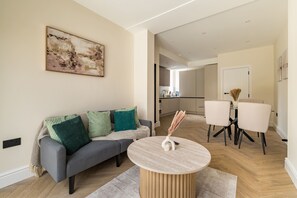 Een moderne woonkamer met een grijze bank, een ronde salontafel en een eethoek met twee stoelen.