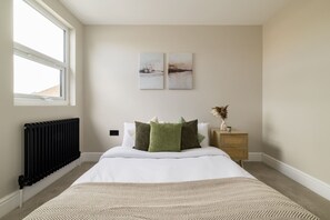 Een slaapkamer met een bed, een radiator, een raam en twee aan de muur hangende schilderijen.
