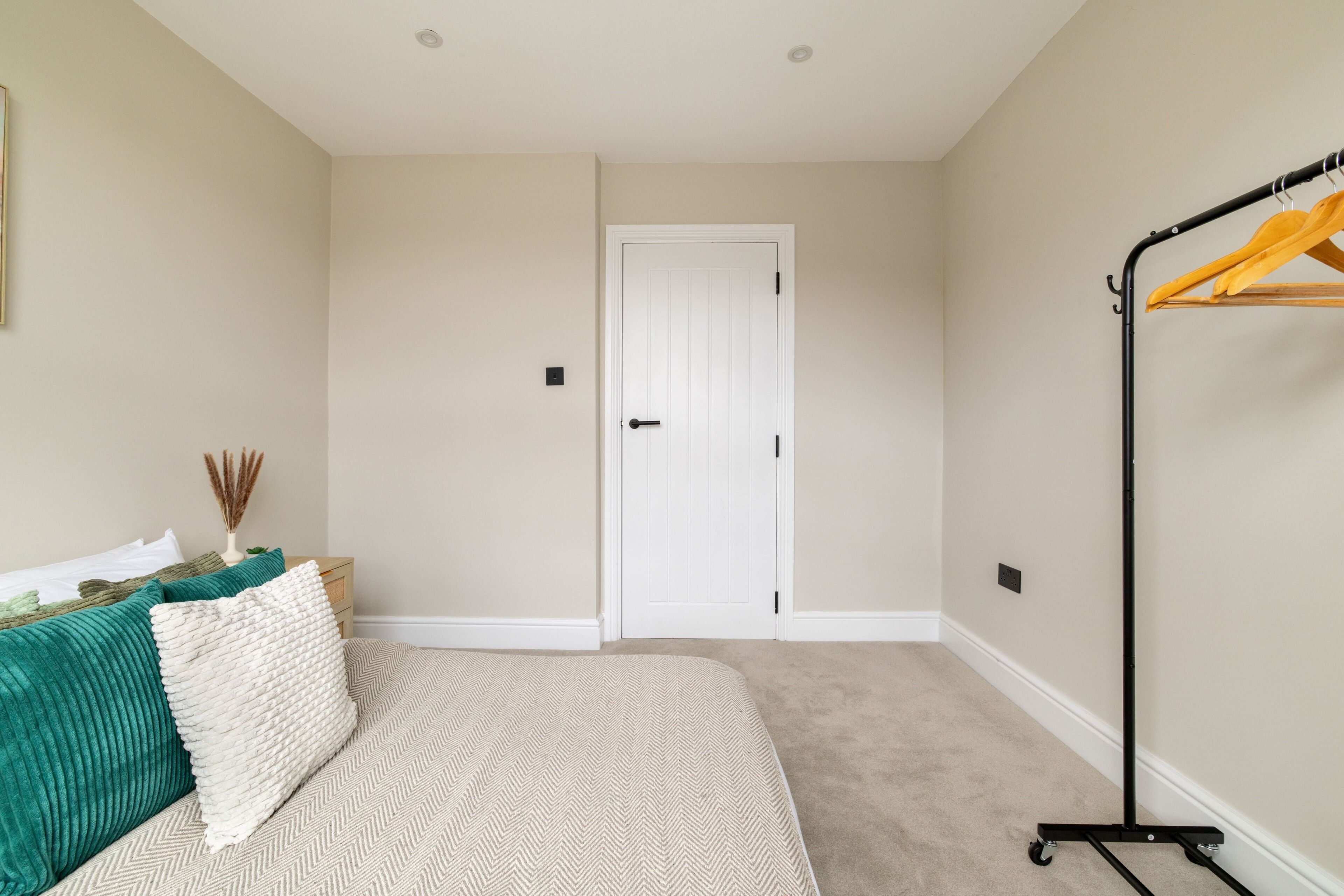 A bedroom with a bed, a white door, a black clothing rack, and a beige carpet.
