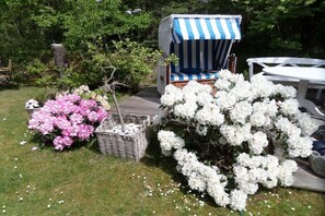 Ein Garten mit einem gestreiften Stuhl, weißen Blumen und einem weißen Tisch.