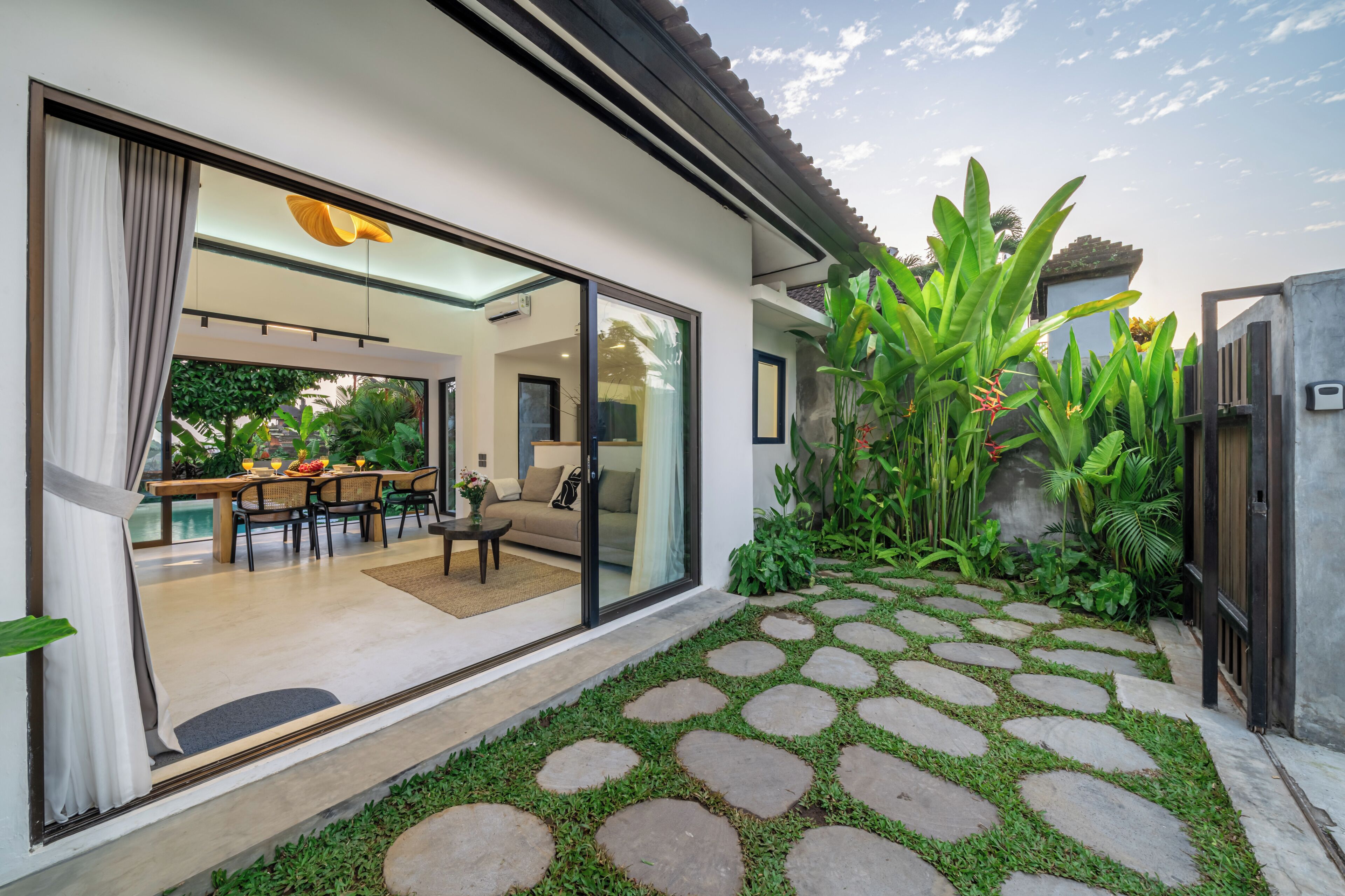 A modern house with a dining area, a sofa, and a garden with stone pathways.