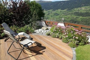 A deck with two lounge chairs, a stone wall, and a view of a valley.