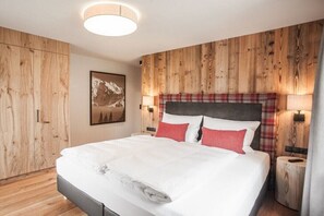 A bedroom with a wooden wall panel, a bed with white bedding and red pillows, a nightstand with a lamp, and a framed picture on the wall.