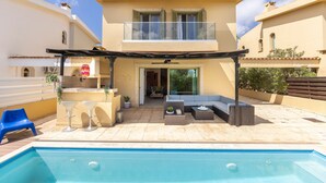 Una casa a due piani con un balcone, una piscina, un'area salotto esterna e un portico coperto.
