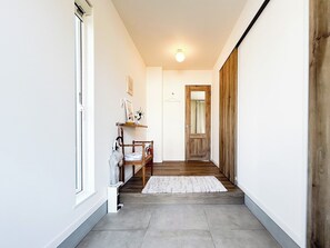 En hall med en trädörr, en vit vägg, en liten hylla med diverse föremål och en matta på golvet.