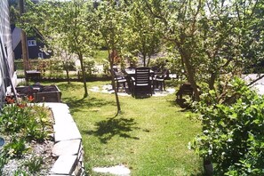 A patio with outdoor furniture, a garden area with plants, and a house in the background. - Holiday home with 4 bedrooms (Burg Reuland)