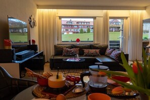 Ein Wohnzimmer mit einer Couch, einem Couchtisch, einem Fernseher und Blick auf ein Gebäude durch ein Fenster.