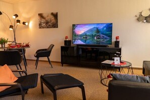 Ein modernes Wohnzimmer mit Flachbildfernseher, schwarzen Möbeln, einem runden Couchtisch und einer Wanddekoration.