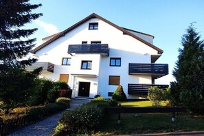 Ein modernes, zweistöckiges Haus mit Balkon, Eingangstür und Auffahrt.
