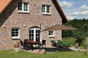 A brick house with a patio, a table with chairs, and a green lounge chair. - Hawthorn in the heathland magic (Bispingen)