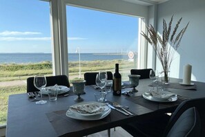 Ein Esstisch für zwei Personen mit Meerblick, eine Weinflasche und eine Vase mit Trockenpflanzen.