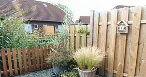 Ein Holzzaun, ein Vogelhaus und Kübelpflanzen in einem Garten.