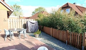 Eine Terrasse mit Tisch und Stühlen, einem überdachten Tisch, einem Blumentopf und einem Holzzaun.