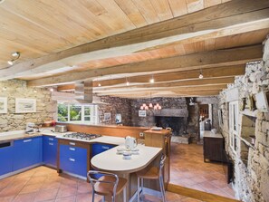 A spacious kitchen with a stone wall, wooden ceiling beams, and a central island with bar stools. - Authentic house for 11, close to the beach (Landéda)