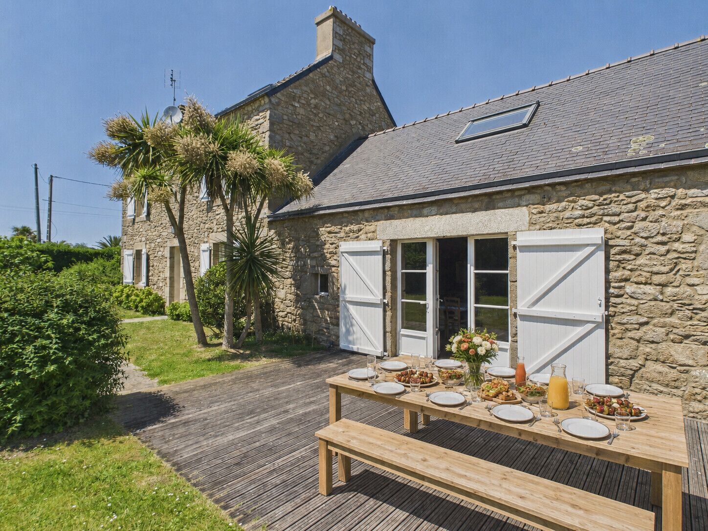 A stone building with a wooden deck, a table set for dining, and a clear sky.