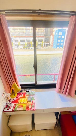 A room with a window overlooking a body of water, a table with a colorful tablecloth, and a pink curtain. - Osaka Dotonbori Riverside Walking distance 5 min / Osaka City Ōsaka (Osaka City)