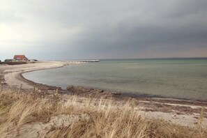 Eine Küstenlandschaft mit Sandstrand, einer Holzsteg und einem Gebäude mit rotem Dach.