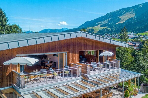 Eine Holzhütte mit Balkon, Sitzgelegenheit im Freien und Blick auf die umliegende Landschaft.