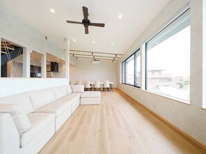 Una sala de estar moderna con un sofá blanco, un ventilador de techo y ventanas amplias.