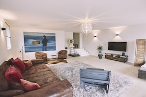 Ein modernes Wohnzimmer mit einer großen Couch, einer Bank, einem Flachbildfernseher und einer Treppe.
