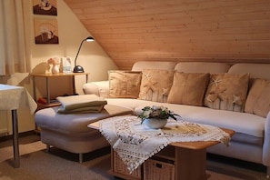 Ein gemütliches Loft-Wohnzimmer mit hohen Decken, einer Couch mit Stichstrahlkissen, einem kleinen Tisch mit Lampe und einer dekorativen Schale darauf.