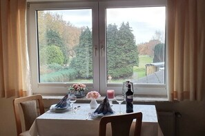 Ein Esstisch für zwei Personen mit Blick auf einen Garten durch ein Fenster.