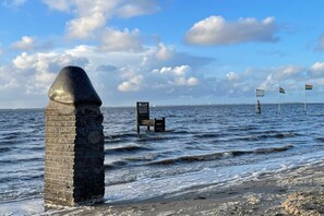 Eine Küstenansicht mit einem Steins Denkmal, einer Bank und Flaggen im Wasser.