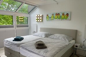 Ein Schlafzimmer mit zwei Betten, einem Oberlicht, einem Gemälde und einem Nachttisch mit einer Lampe.