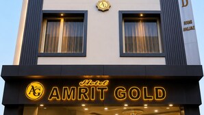 Um hotel chamado 'Amrit Gold', com fachada moderna, várias janelas e uma placa indicando quartos disponíveis.