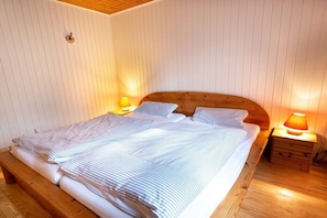 A single bed with a wooden headboard, two bedside lamps, and a wooden bench at the foot of the bed. - Holiday home with 2 bedrooms (Böddenstedt)