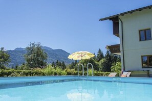 Ein Swimmingpool mit Blick auf die Berge, eine Liege und ein Sonnenschirm.