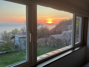 A view through a window with a view of a sunset over water, trees, and a building.