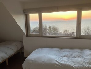 Una habitación con cama y ventana que da a una masa de agua durante el atardecer.