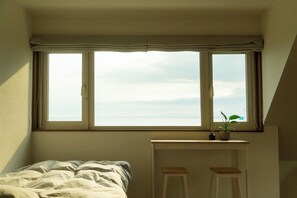 Une chambre avec une grande fenêtre, un lit, une petite table et une plante en pot.