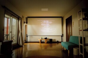 Une pièce dotée d’un écran de projection affichant du texte, d’une table en bois, d’un canapé de couleur turquoise et d’une fenêtre avec des rideaux.