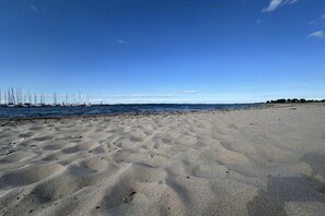 Ein sandiger Strand mit Booten im Wasser und wolkenlosem Himmel.