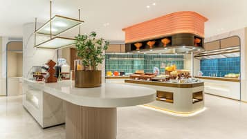 A modern hotel lobby with a central reception desk, a decorative plant, and a large orange accent wall.
